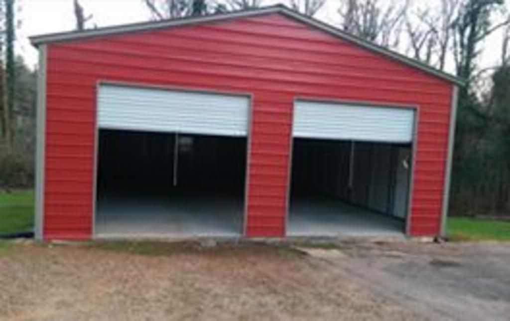 A red garage with two roller doors is sitting on the side of a dirt road.