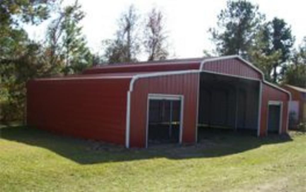 A red barn is sitting in the middle of a grassy field.