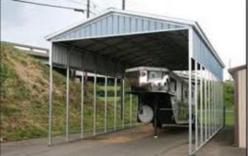 A trailer is parked under a metal carport.