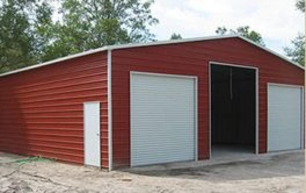 A red garage with white doors is sitting in the middle of a dirt field.