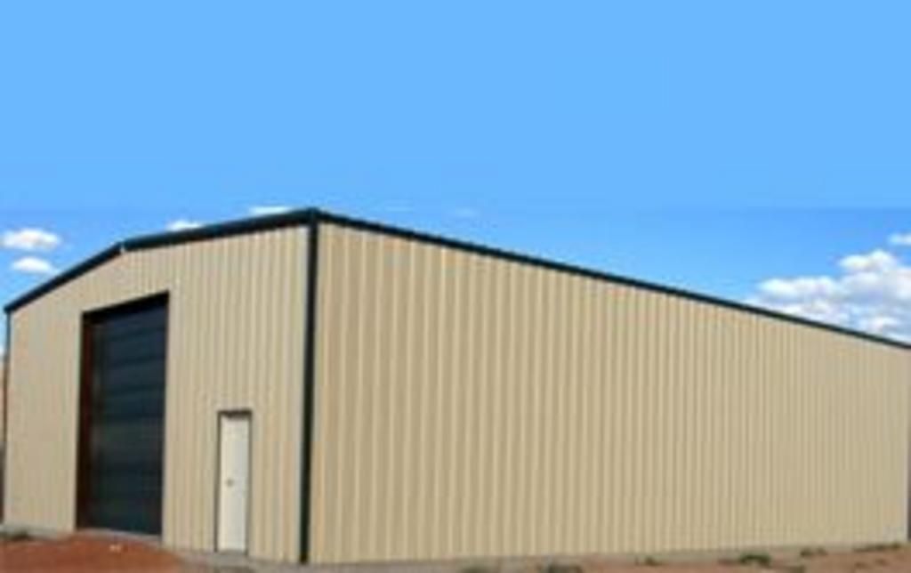 A large tan metal building with a black door and a blue sky in the background.