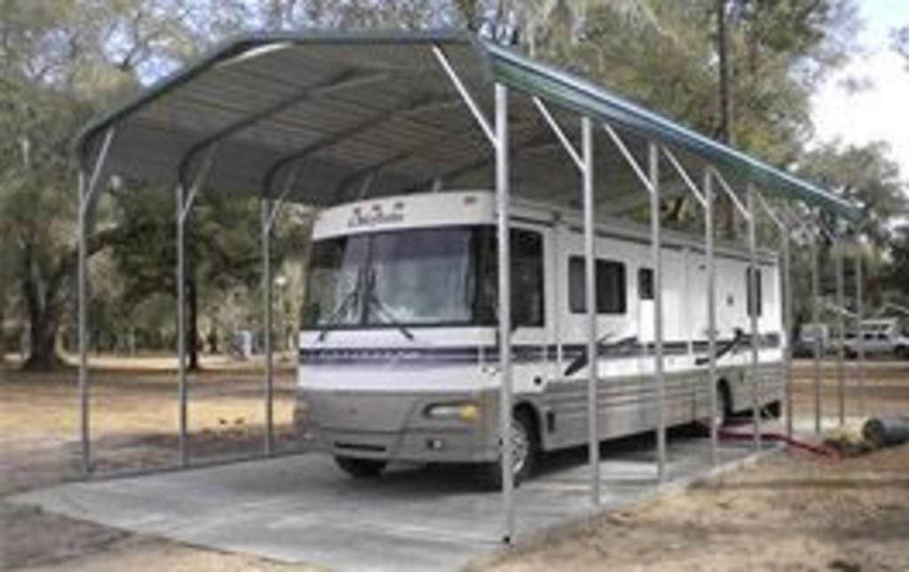 A rv is parked under a carport with trees in the background