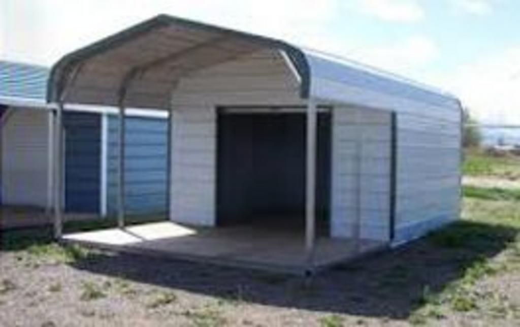 A small metal building with a canopy is sitting in the middle of a field.