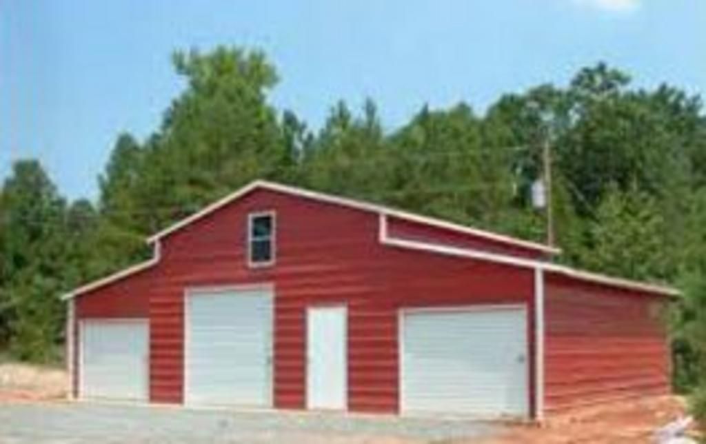 A red barn with white doors is sitting on top of a dirt field.