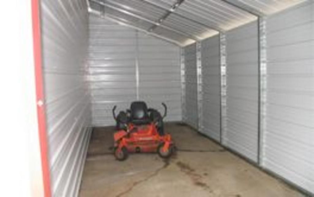 An orange lawn mower is parked in a shed.