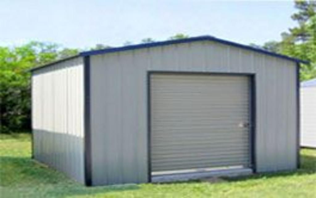 A metal shed with a roll up door is sitting in the middle of a grassy field.