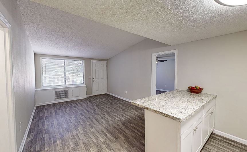 Photo of a living room, seen from the kitchen, with the entrance to a bedroom in the middleground