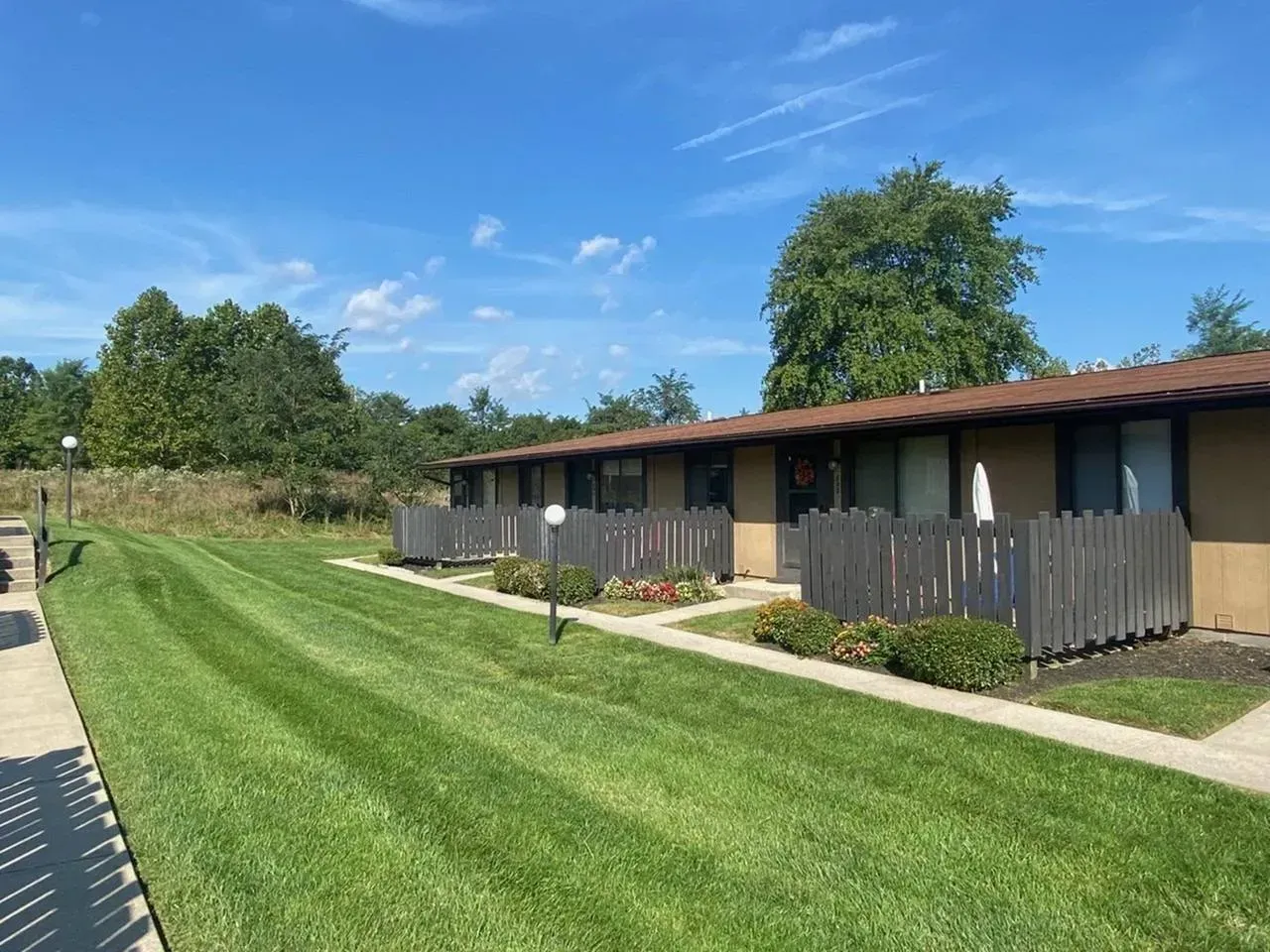 A row of brown-roofed apartments with brown fences, green lawn, and blue sky.
