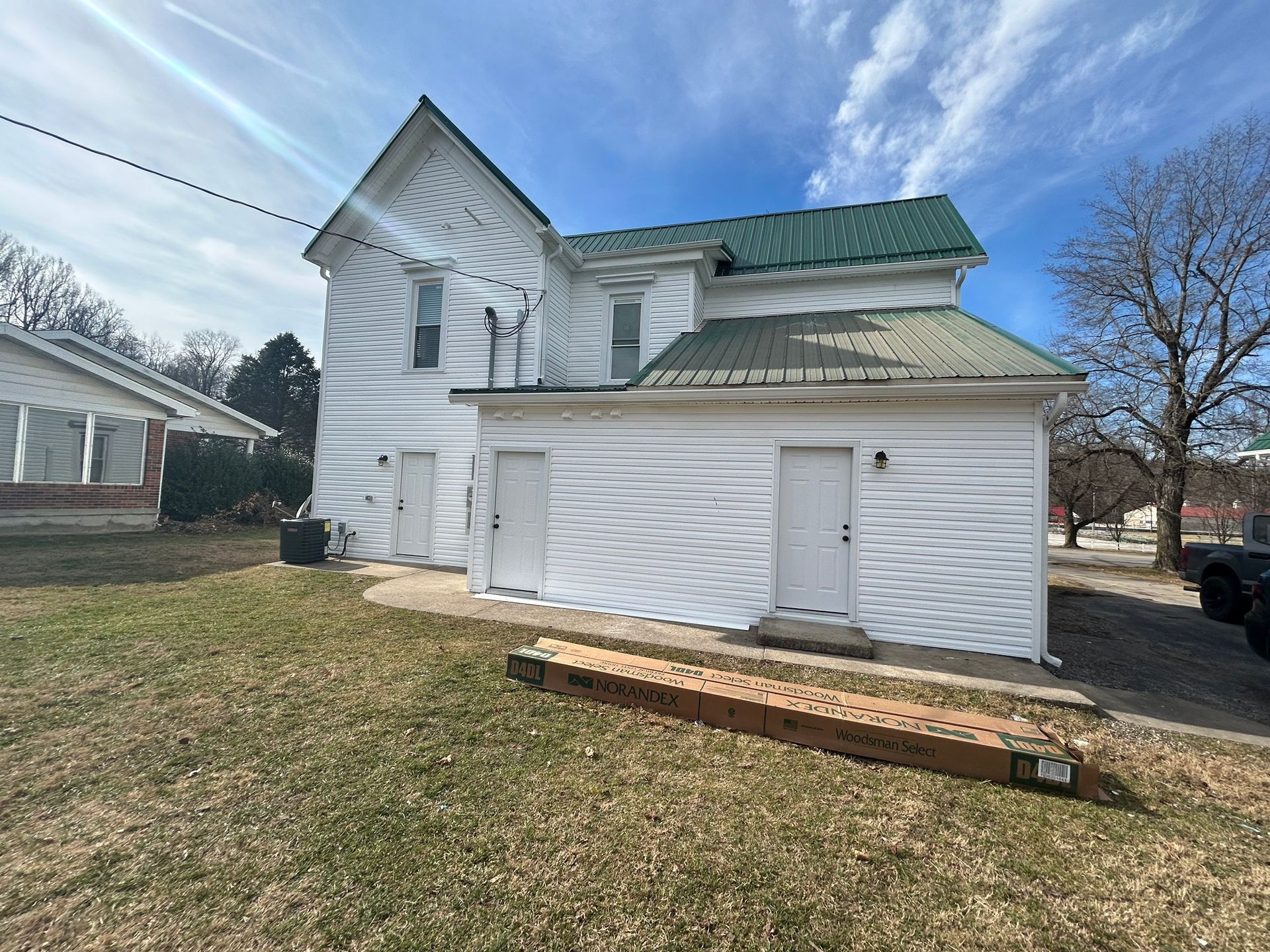 A white house with a green roof is sitting on top of a lush green field.