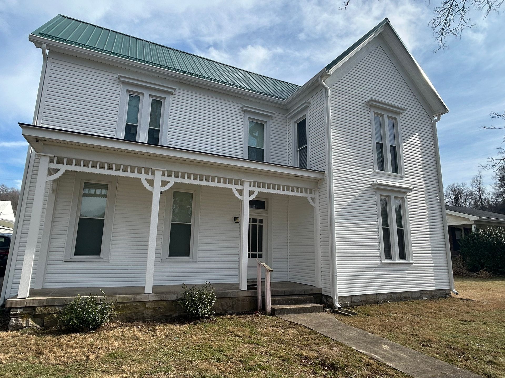 A white house with a green roof and a porch.