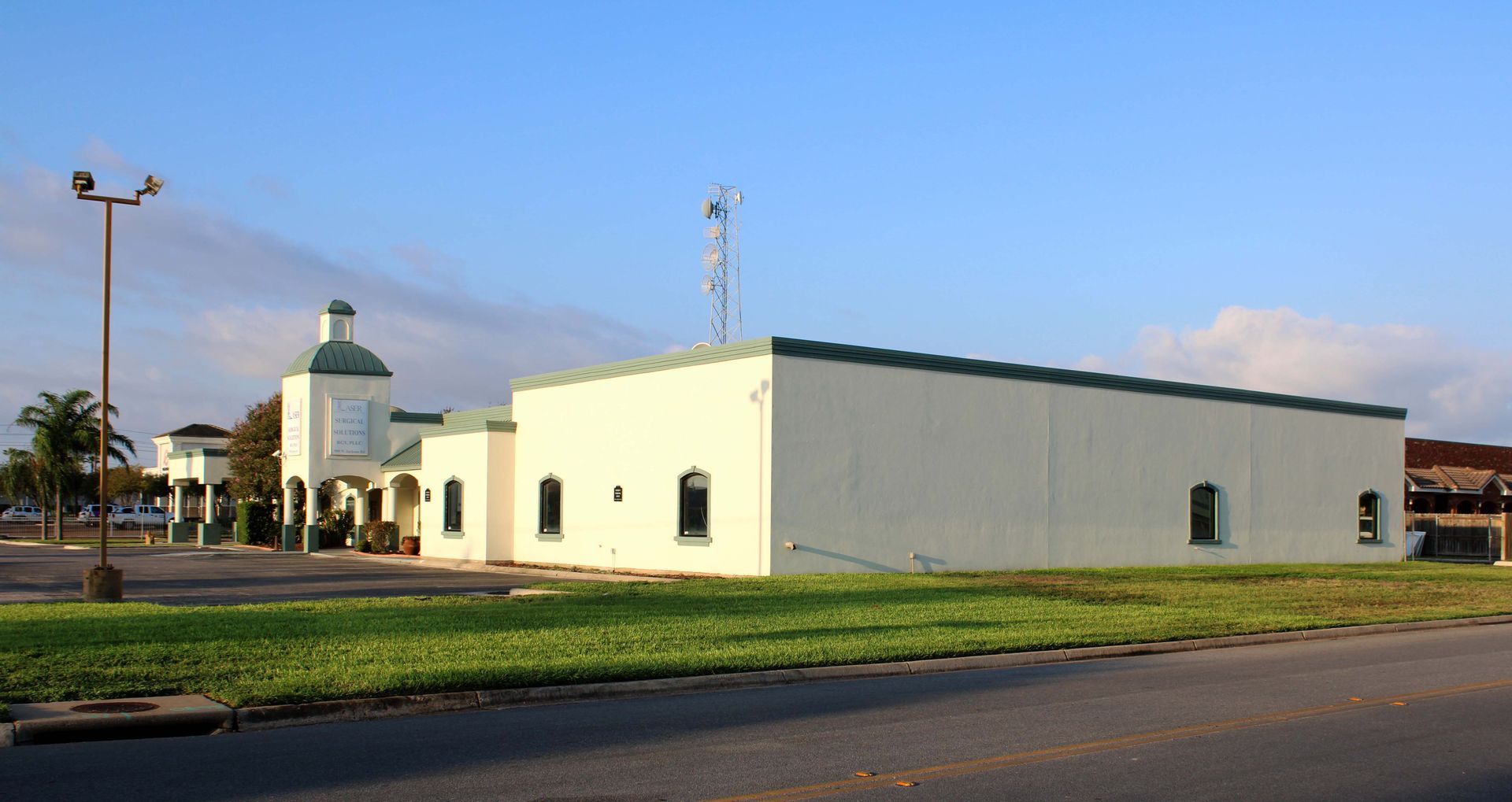 A white building with a green roof is sitting in the middle of a grassy field.
