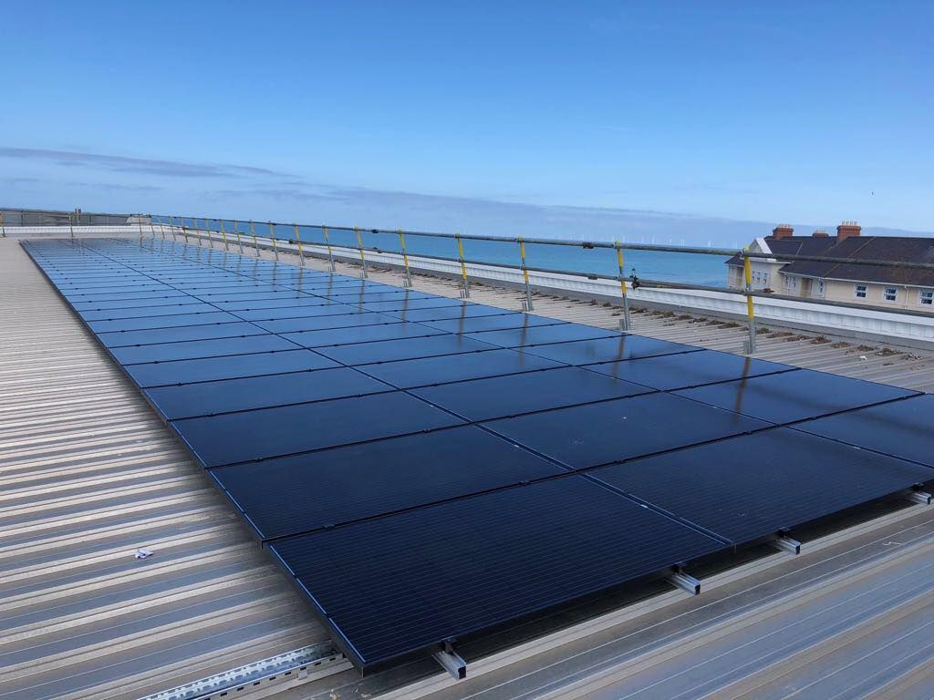 Solar panels on a rooftop beside the sea under a clear blue sky.