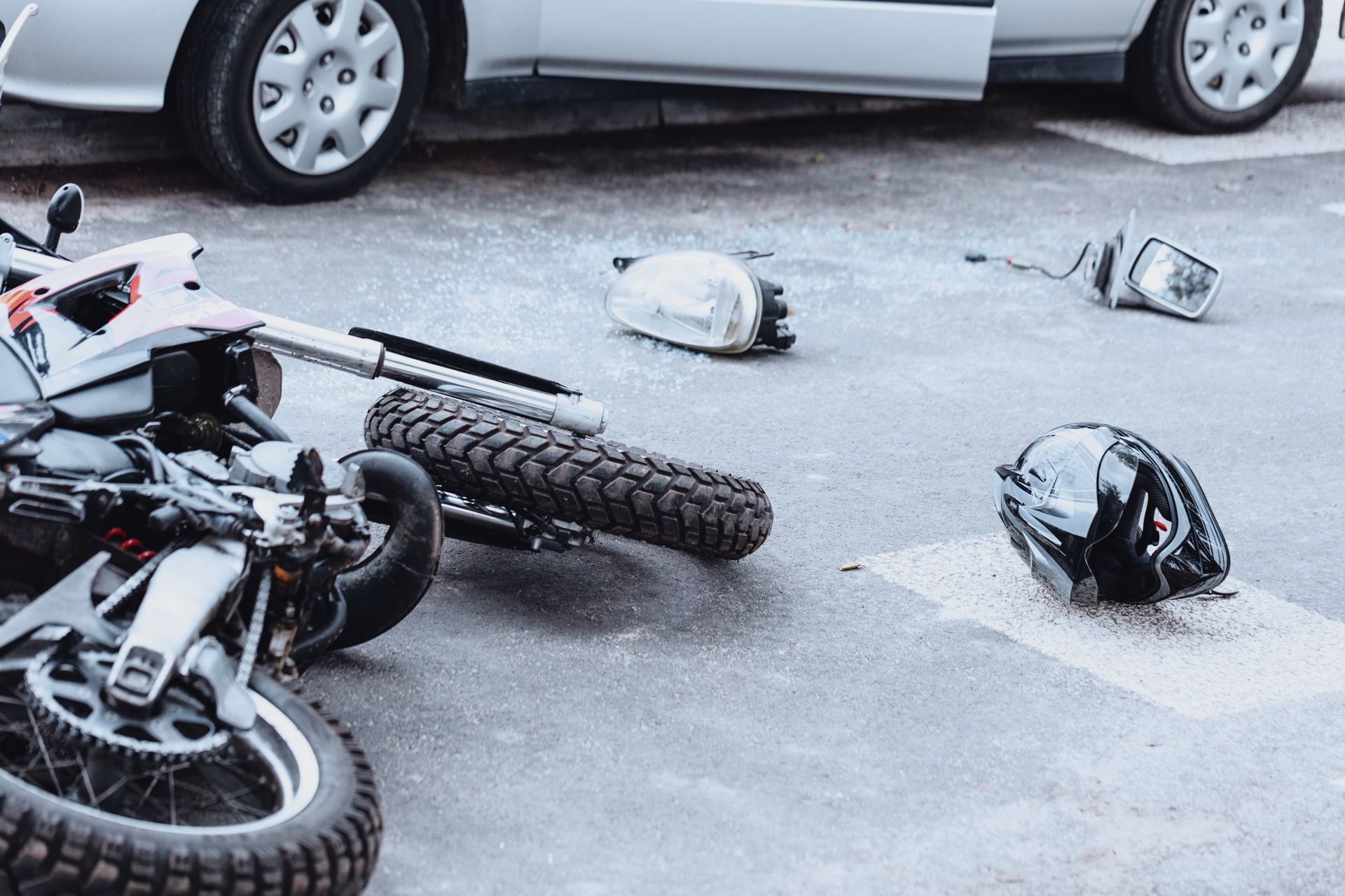 A motorcycle has crashed into a car on the side of the road.