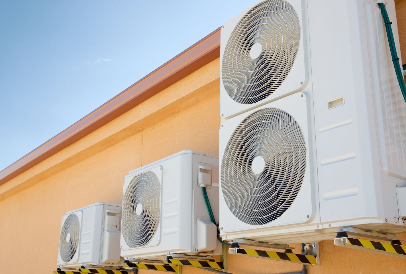 Three air conditioners are lined up on the side of a building.