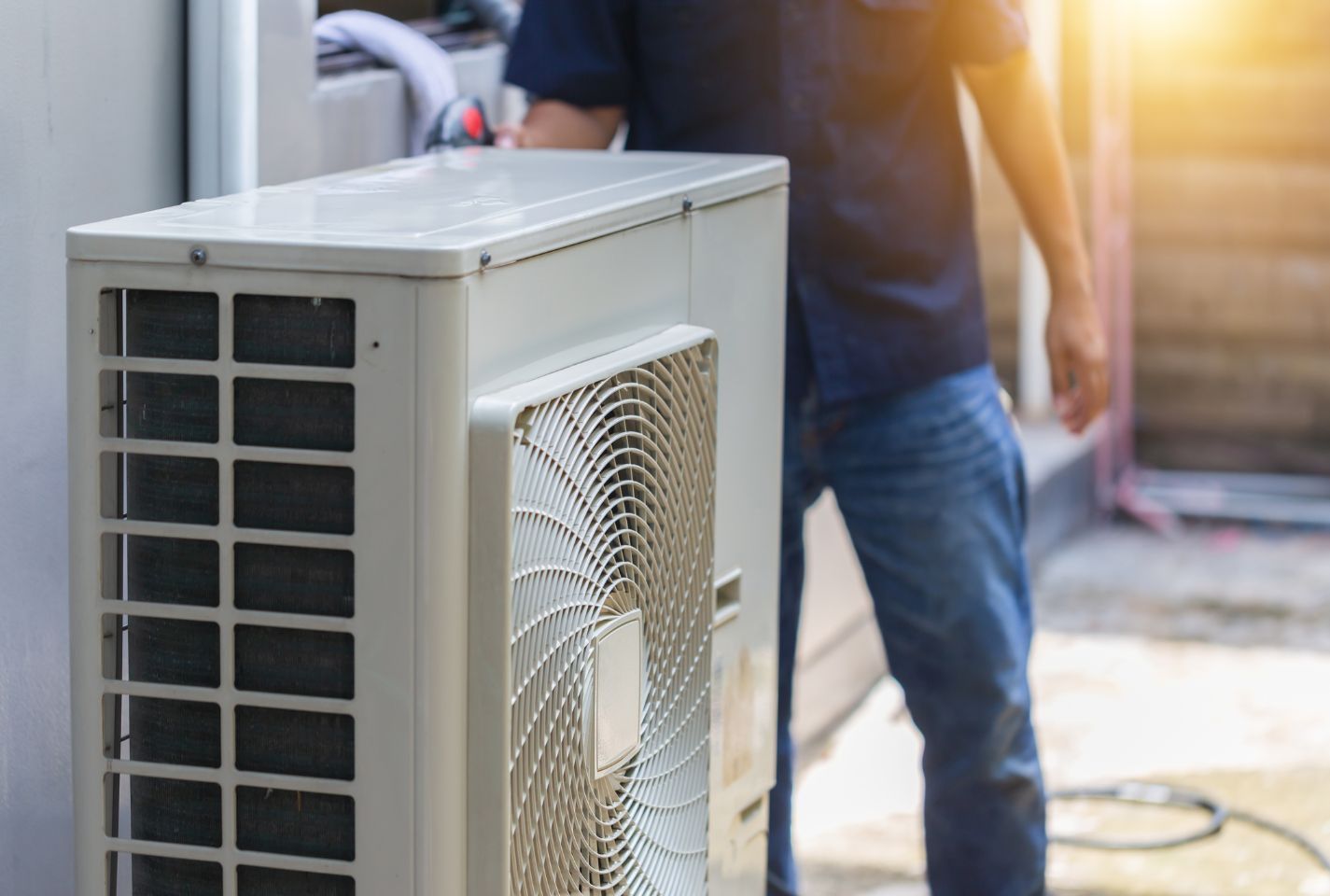 A man is working on an air conditioner outside of a building.