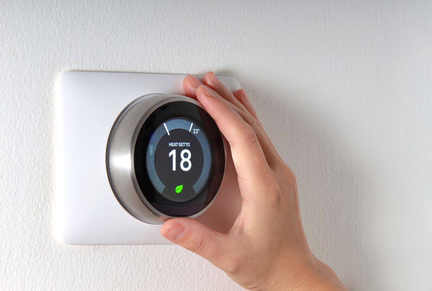 A person is adjusting a smart thermostat on a wall.