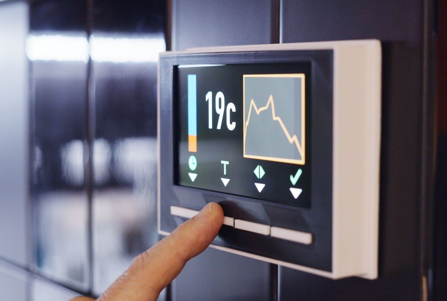 A person is pressing a button on a thermostat that says 19 degrees celsius