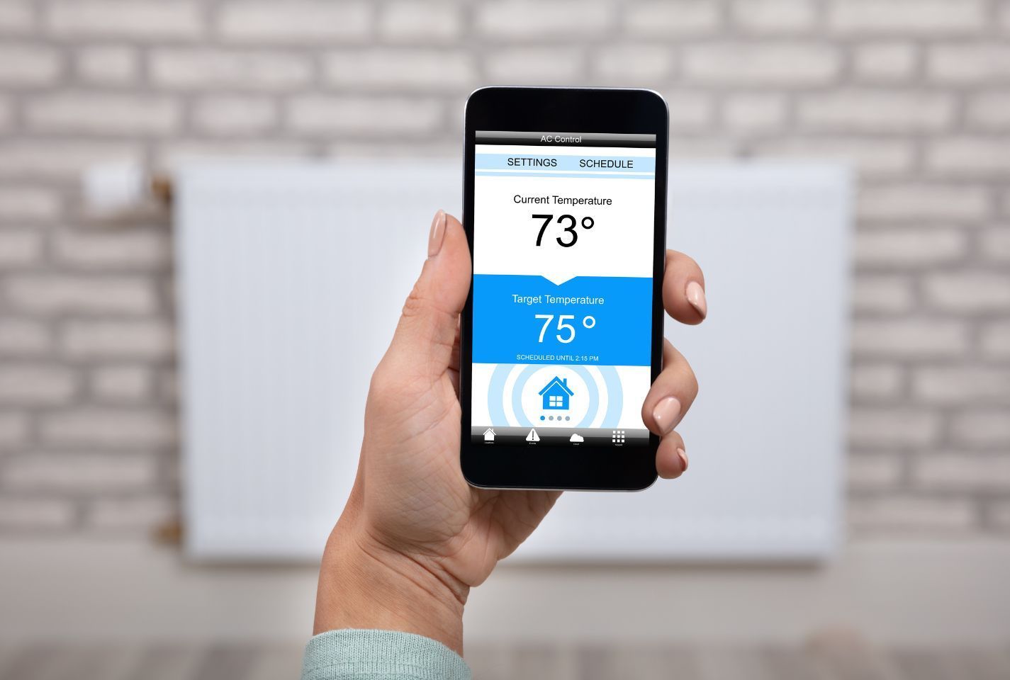 A person is holding a smart phone in front of a thermostat.