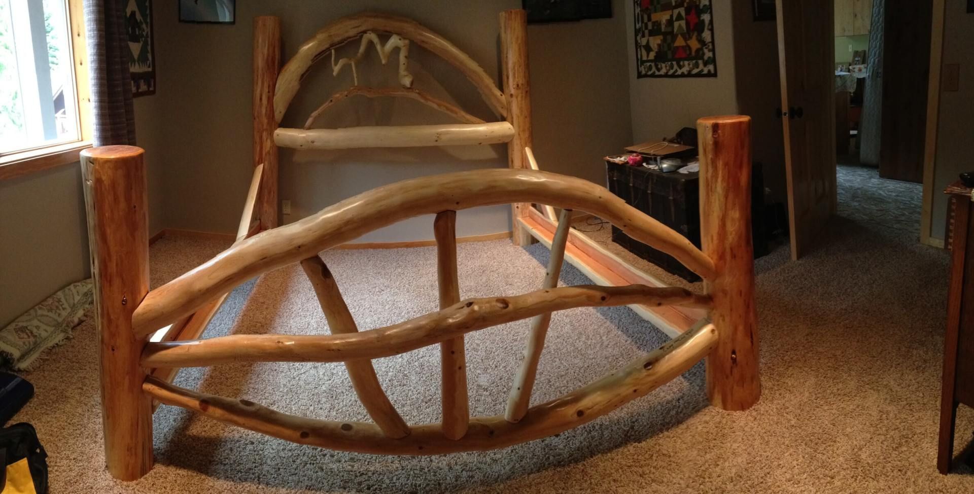 Rustic wooden bed frame in a bedroom with natural wood posts and curved headboard.