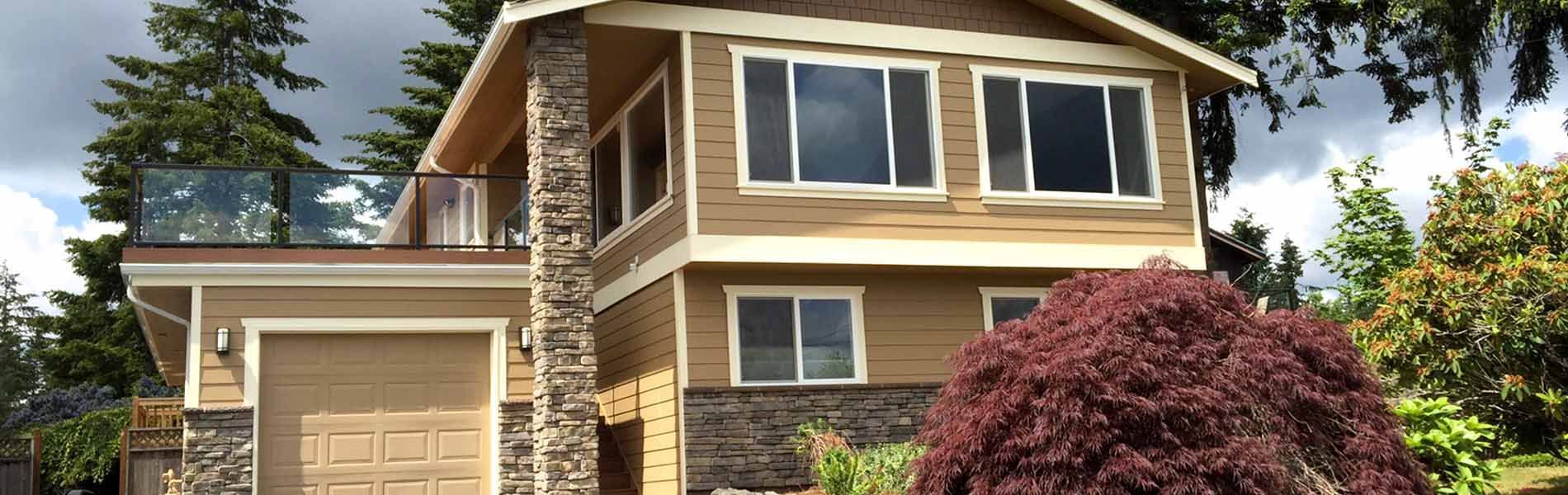 Two-story tan house with stone accents, a garage, and a balcony. A red bush sits in the front yard.