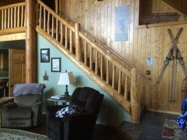Wooden staircase in a cabin, light wood walls, two armchairs, lamp, artwork, skis, a mezzanine.
