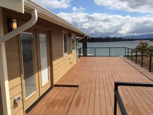 Tan house with a brown deck overlooking a lake and cloudy sky.