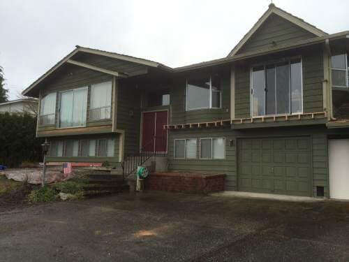 Green house with multiple levels, windows, and attached garage. Brick steps lead to a red front door.