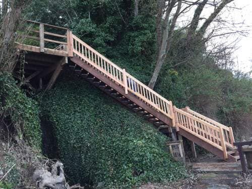 Wooden staircase built into a hillside, leading down to a wooded area.