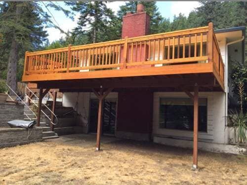 Wooden deck over a home's lower level, supported by posts. The deck has a railing, and the house has a red chimney.