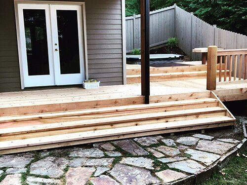 Wooden deck with steps leading to a house with white French doors; stone path in the foreground.