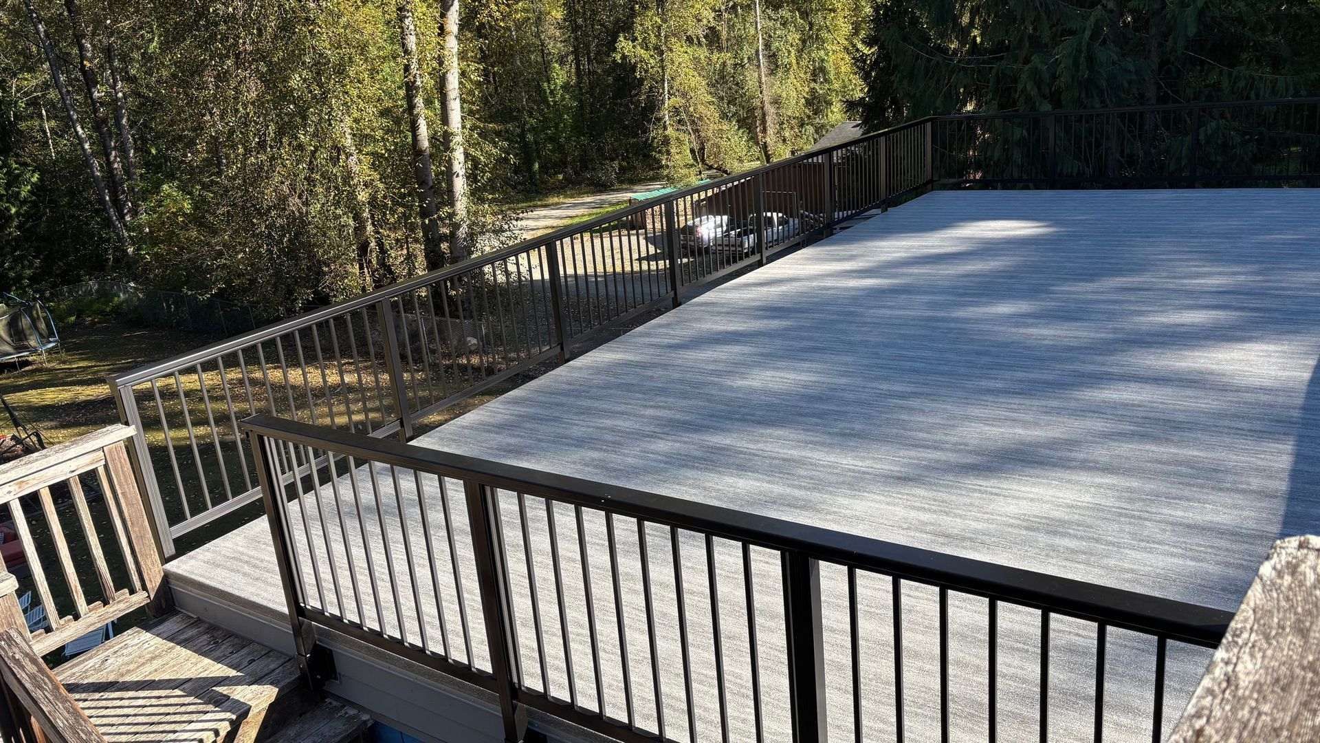 A large, gray concrete deck with dark metal railings overlooking a wooded area.