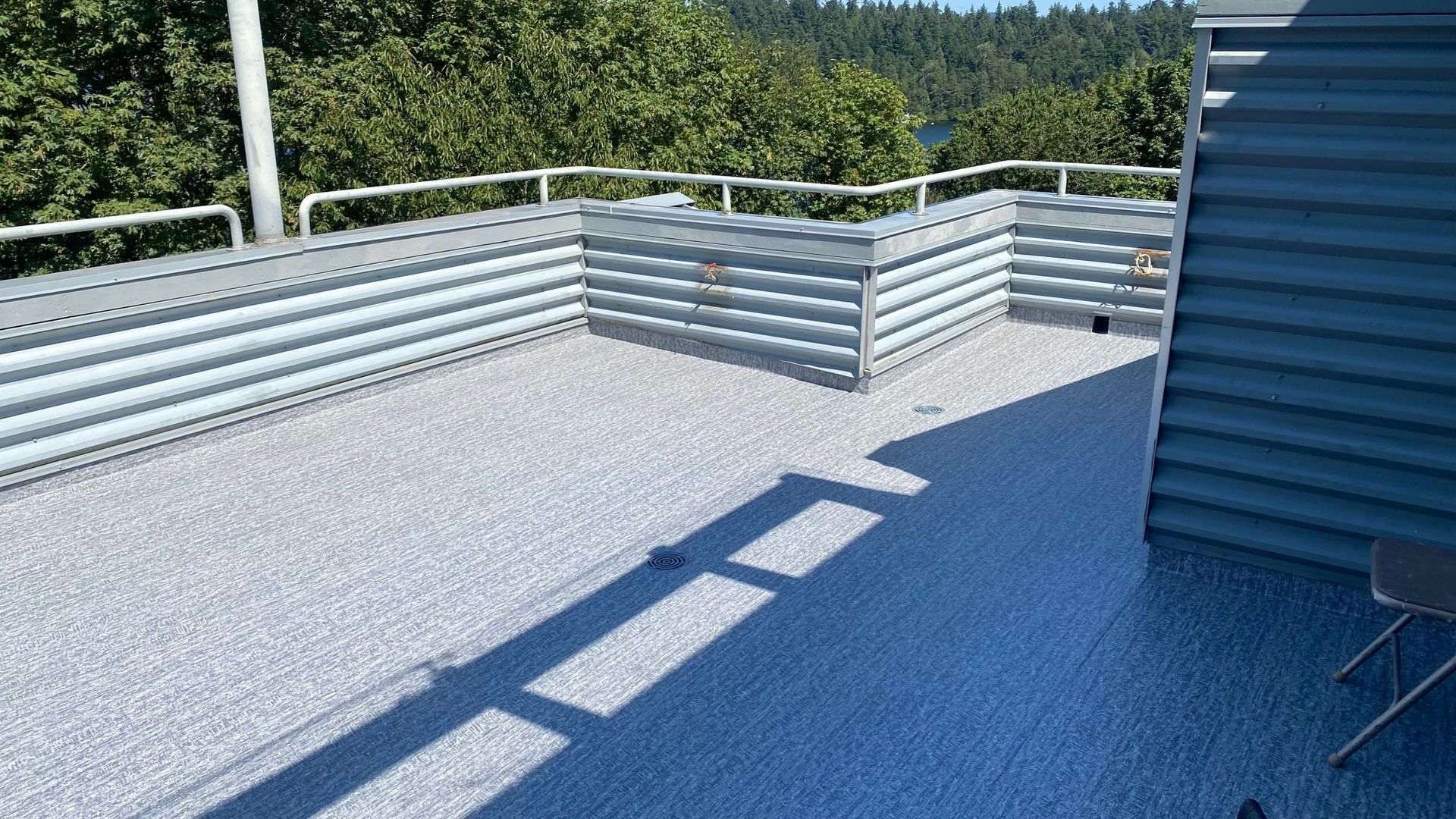 Rooftop deck with gray corrugated metal planters and railing, overlooking trees and a body of water.