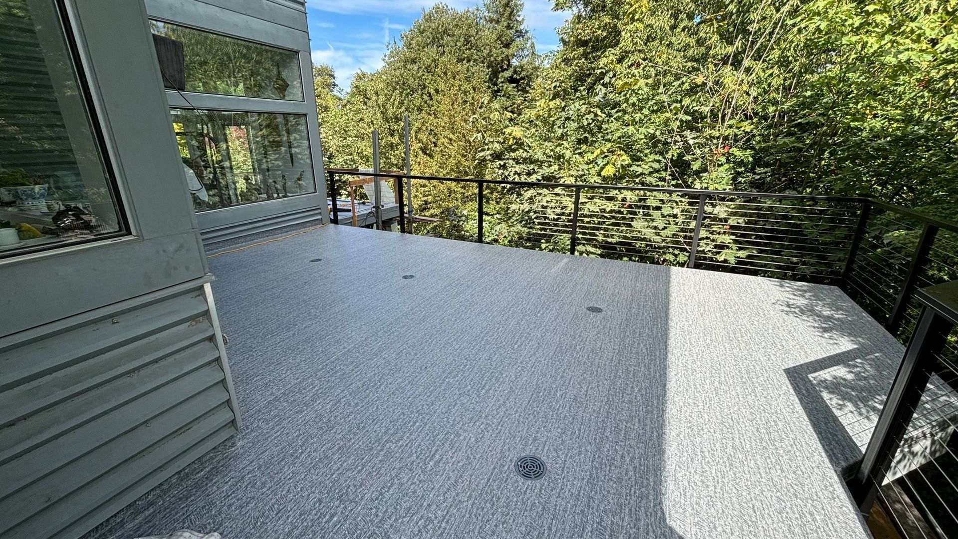 Grey speckled deck with black railing overlooking trees.