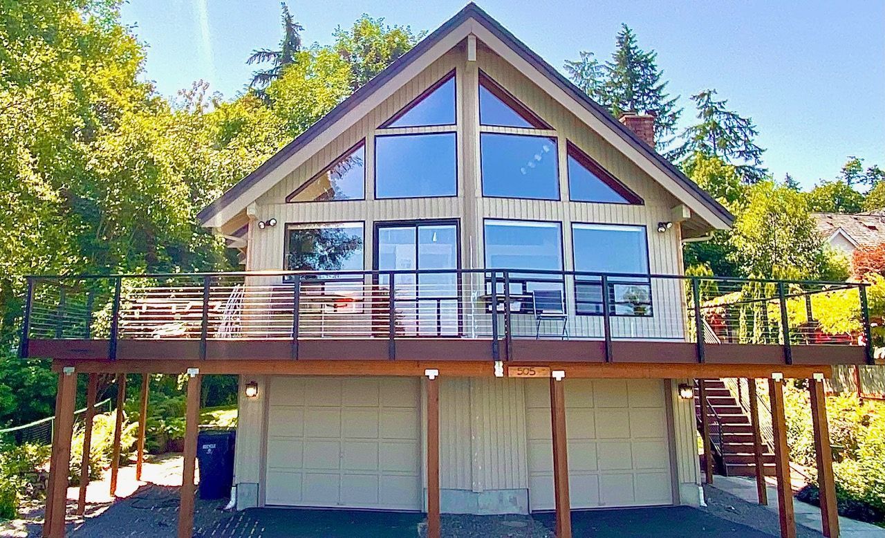 Green ranch-style house with gray driveway and garage, surrounded by bushes and trees.