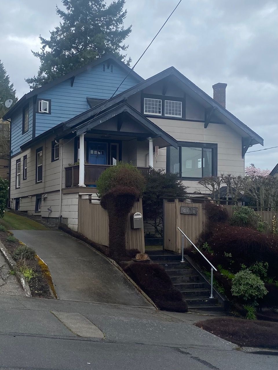 Two-story house with blue upper section and tan lower section, on a slight hill. A driveway and steps lead to the entrance.