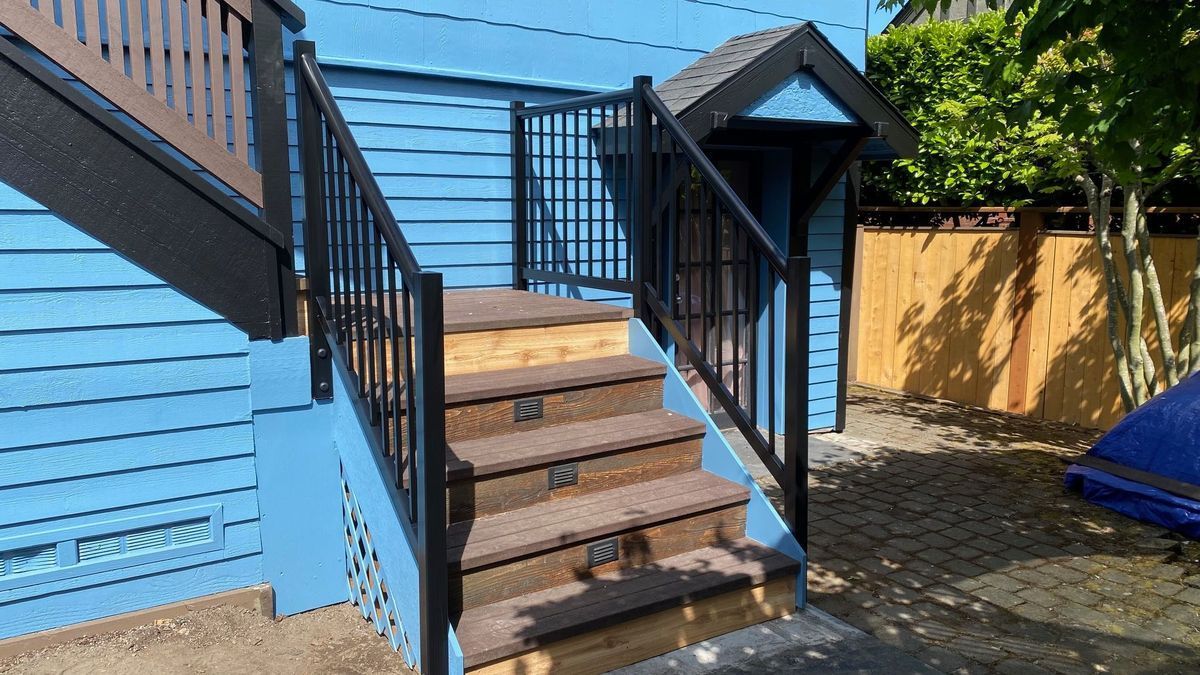 Exterior staircase with black railing and brown steps leading to a blue building.