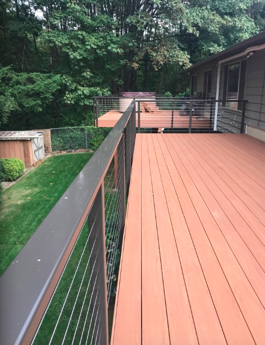 Deck with rust-colored boards and metal railing overlooking a grassy yard and trees.