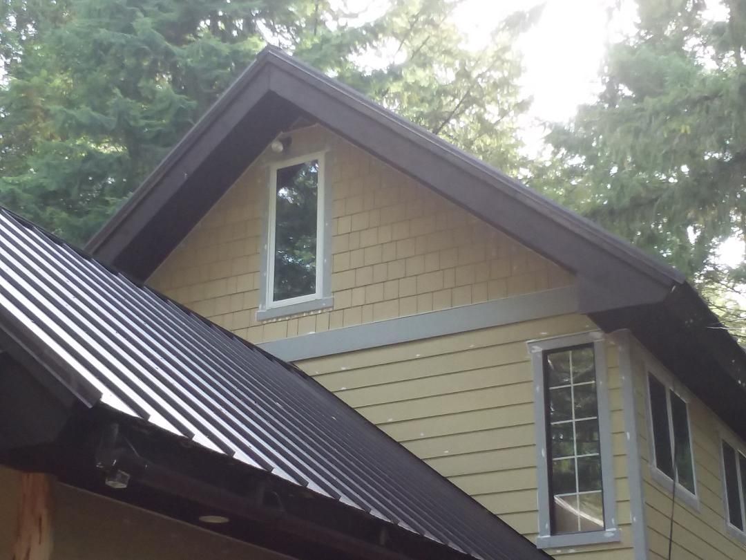 House exterior with metal roof, tan siding, and brown trim, windows, and gutter system.