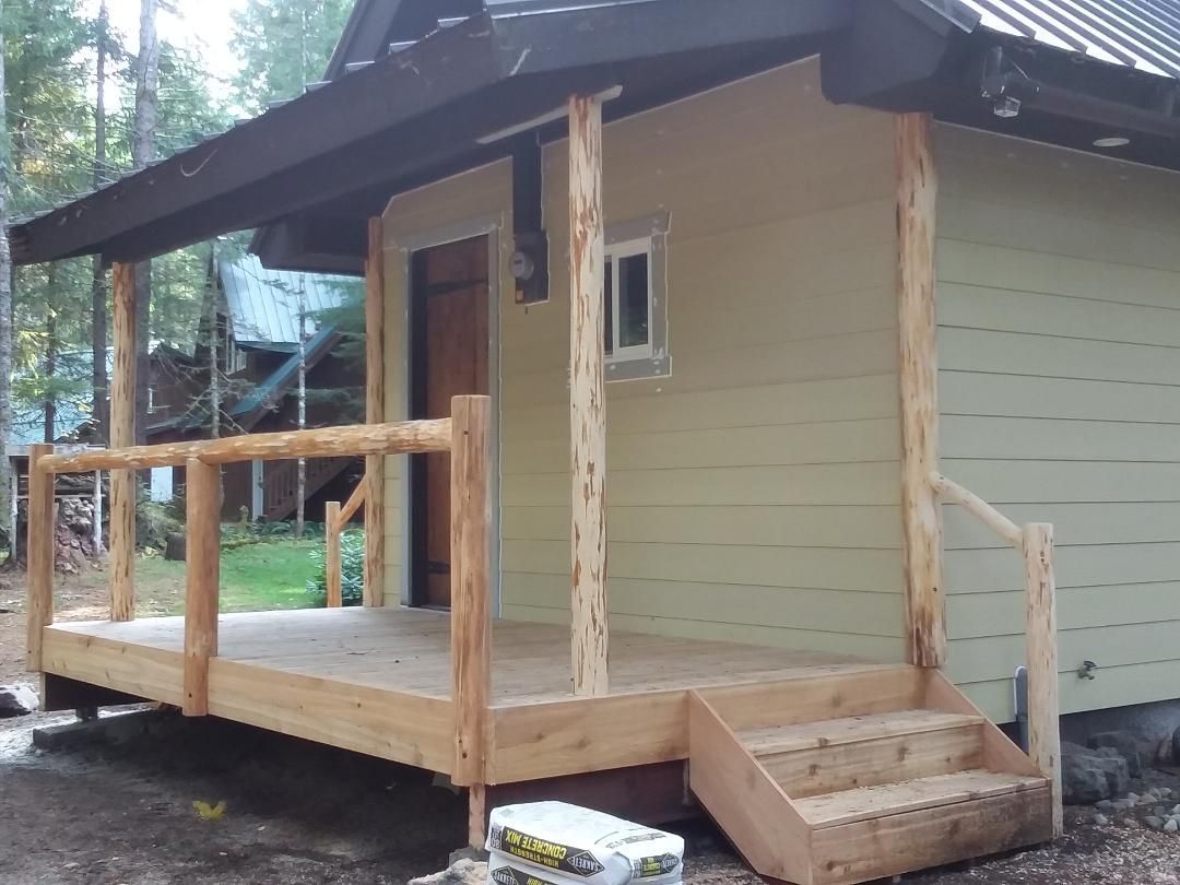 Cabin with wooden porch, steps, and railing. Beige siding, dark roof, doorway, small window.