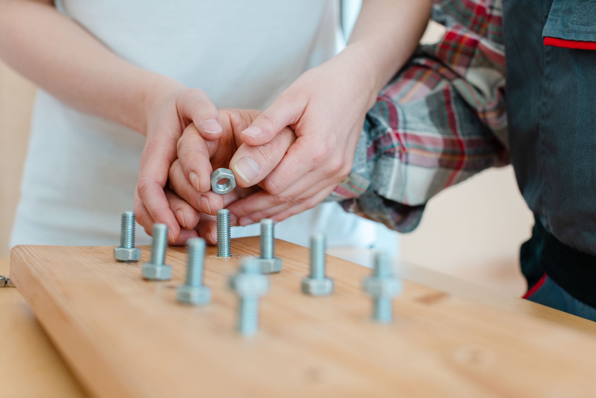 Hands holding a nut, placing it on a bolt attached to a wooden board.