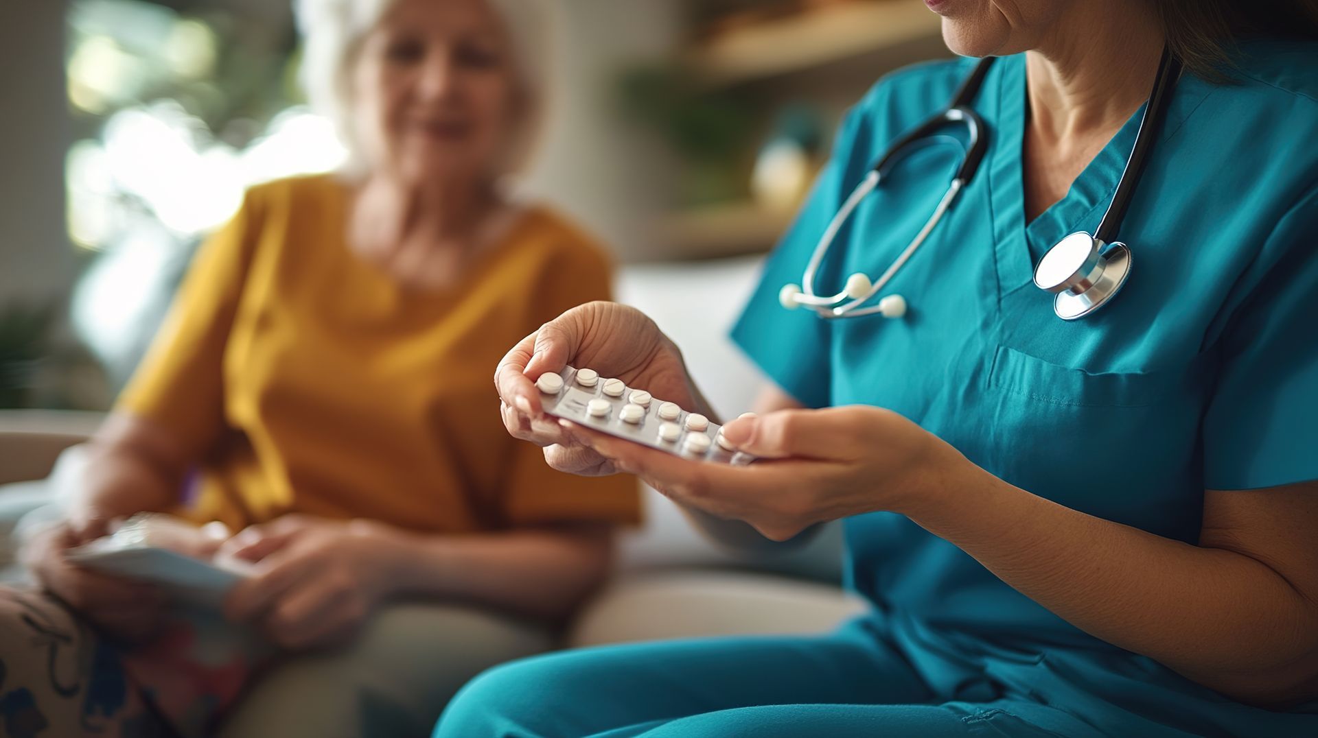 Nurse showing pills to an elderly woman seated indoors; doctor wearing blue scrubs and stethoscope.