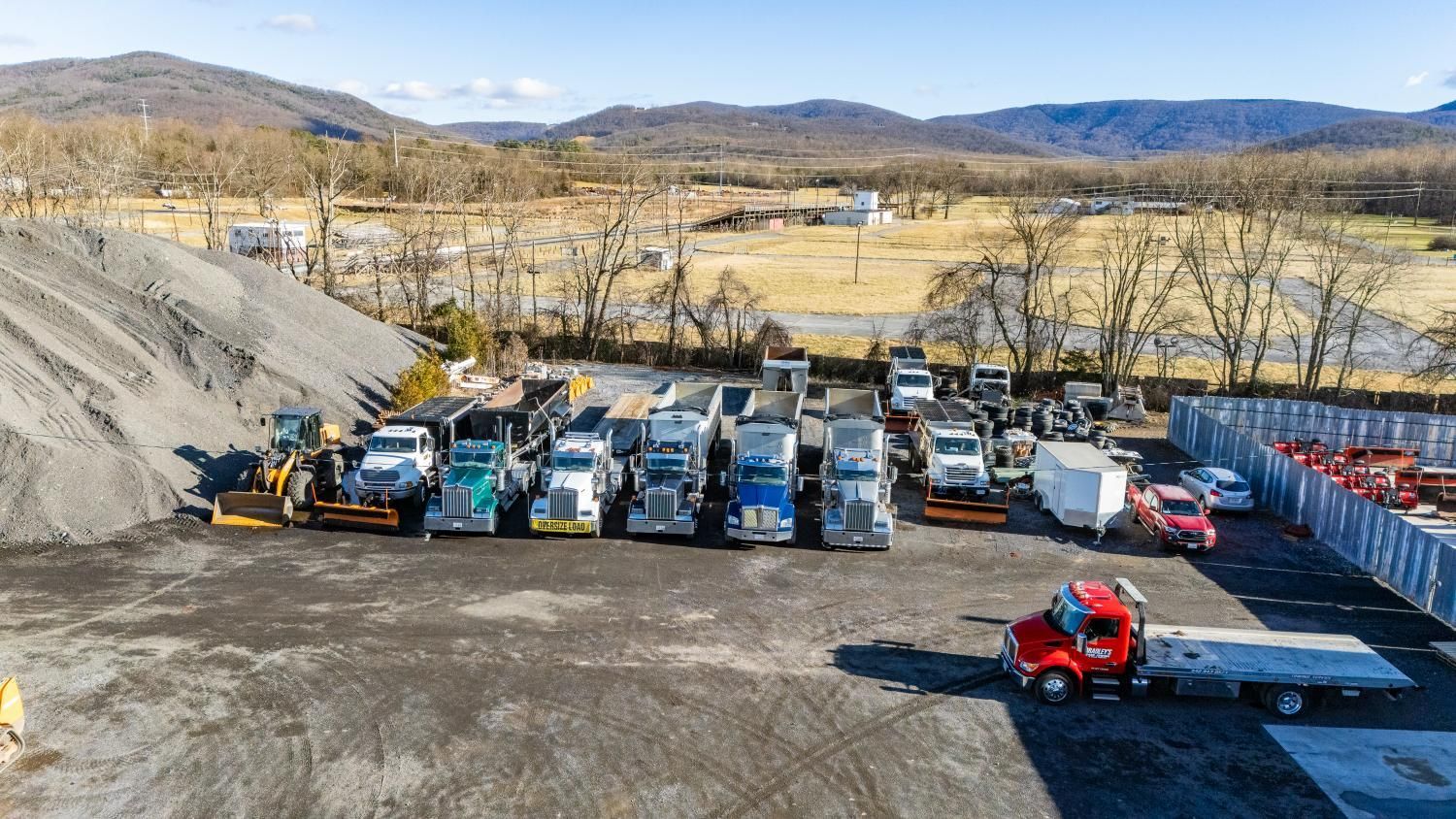 A bunch of trucks are parked in a lot with mountains in the background.