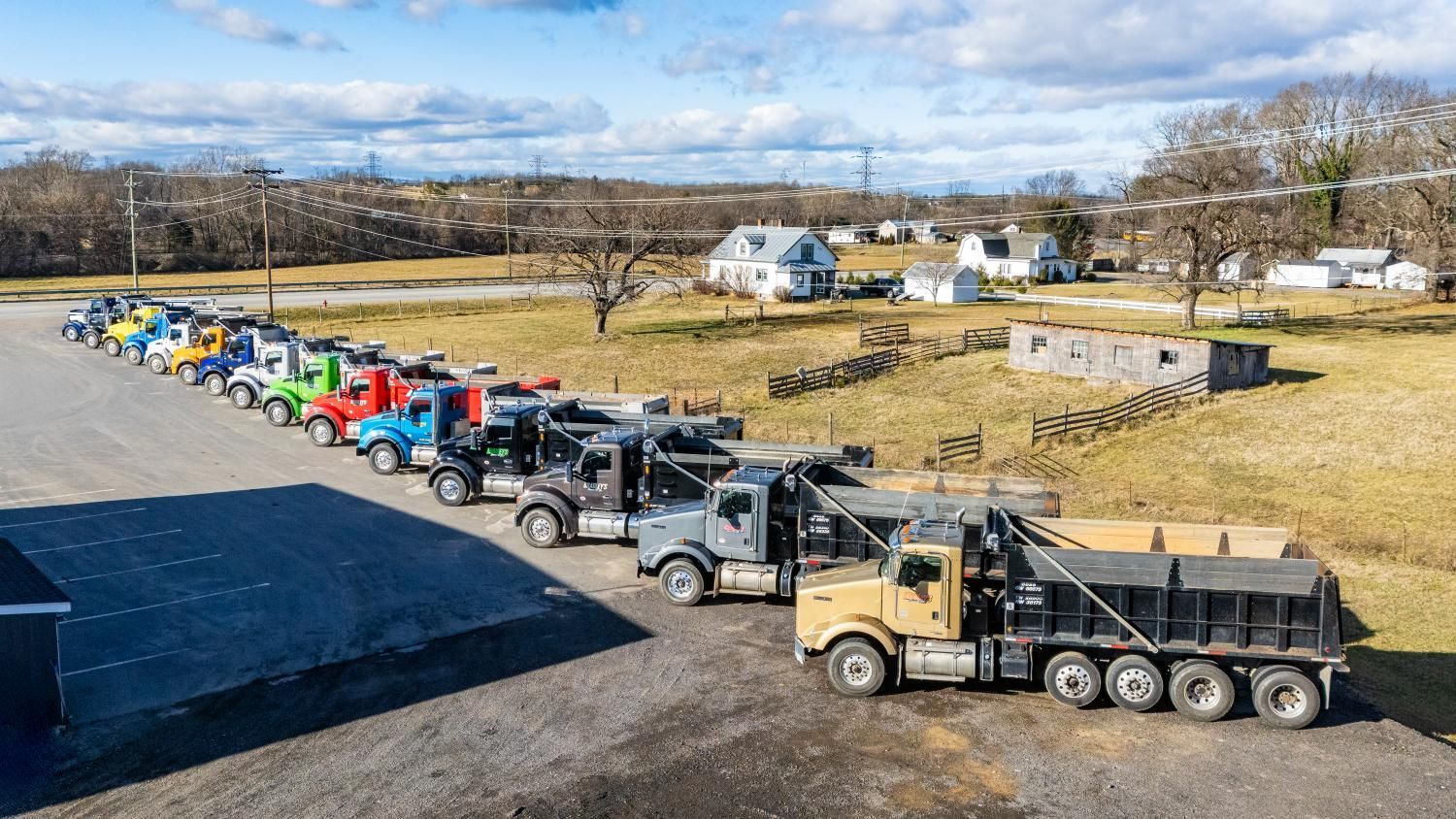 A row of dump trucks are parked in a parking lot.