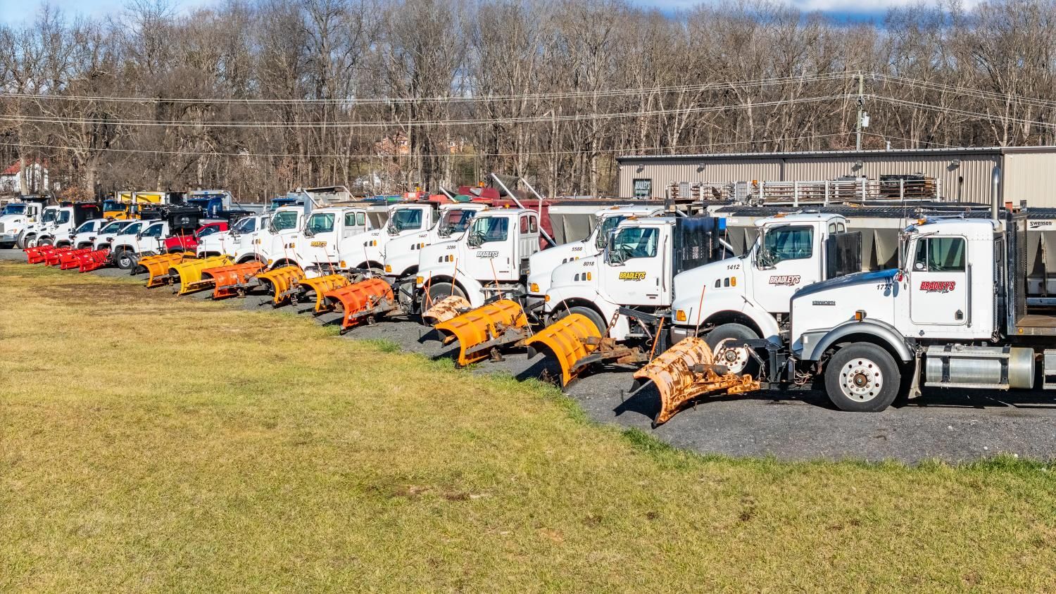 A row of snow plows are parked in a field.