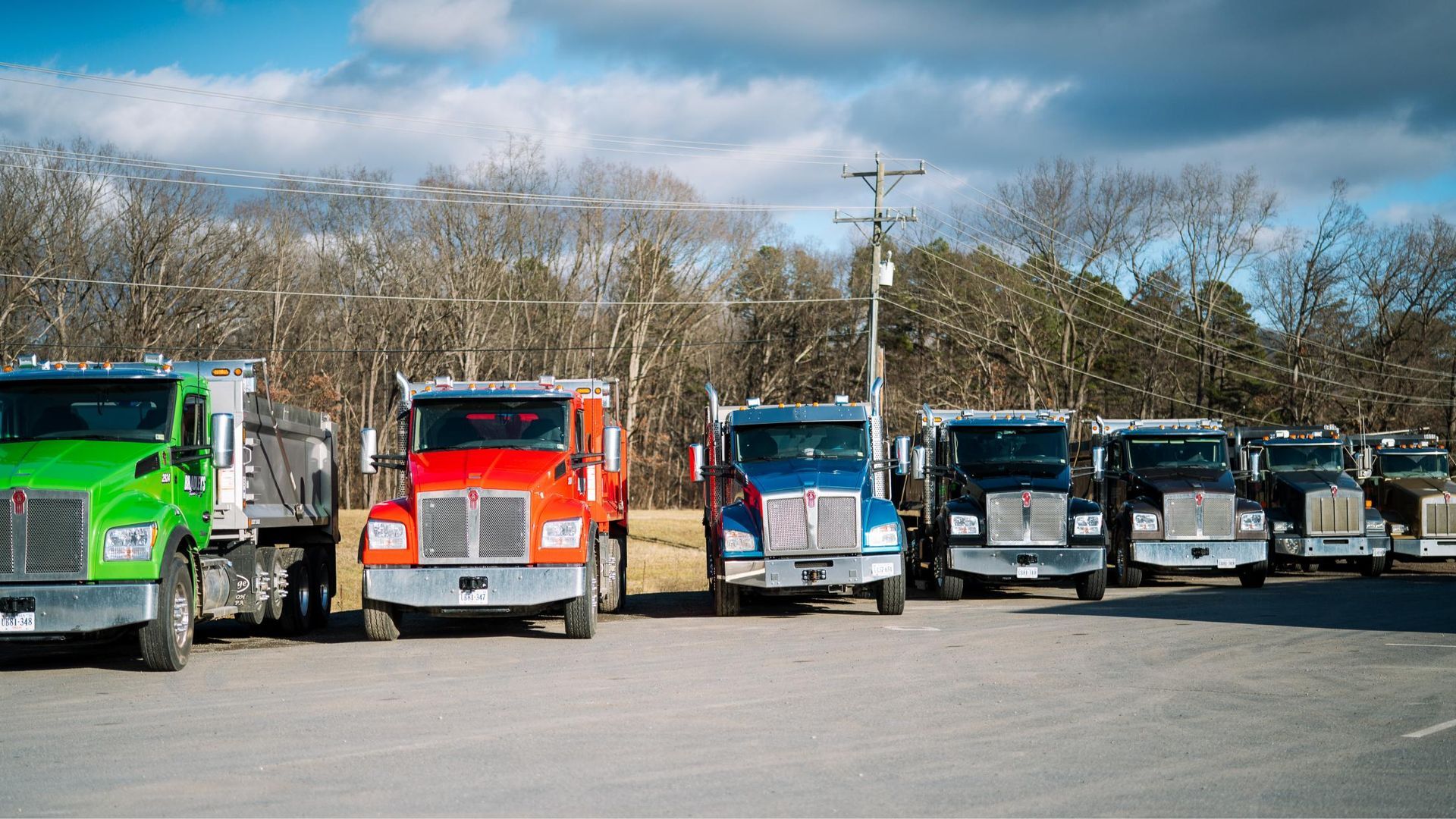 A row of dump trucks are parked in a parking lot.