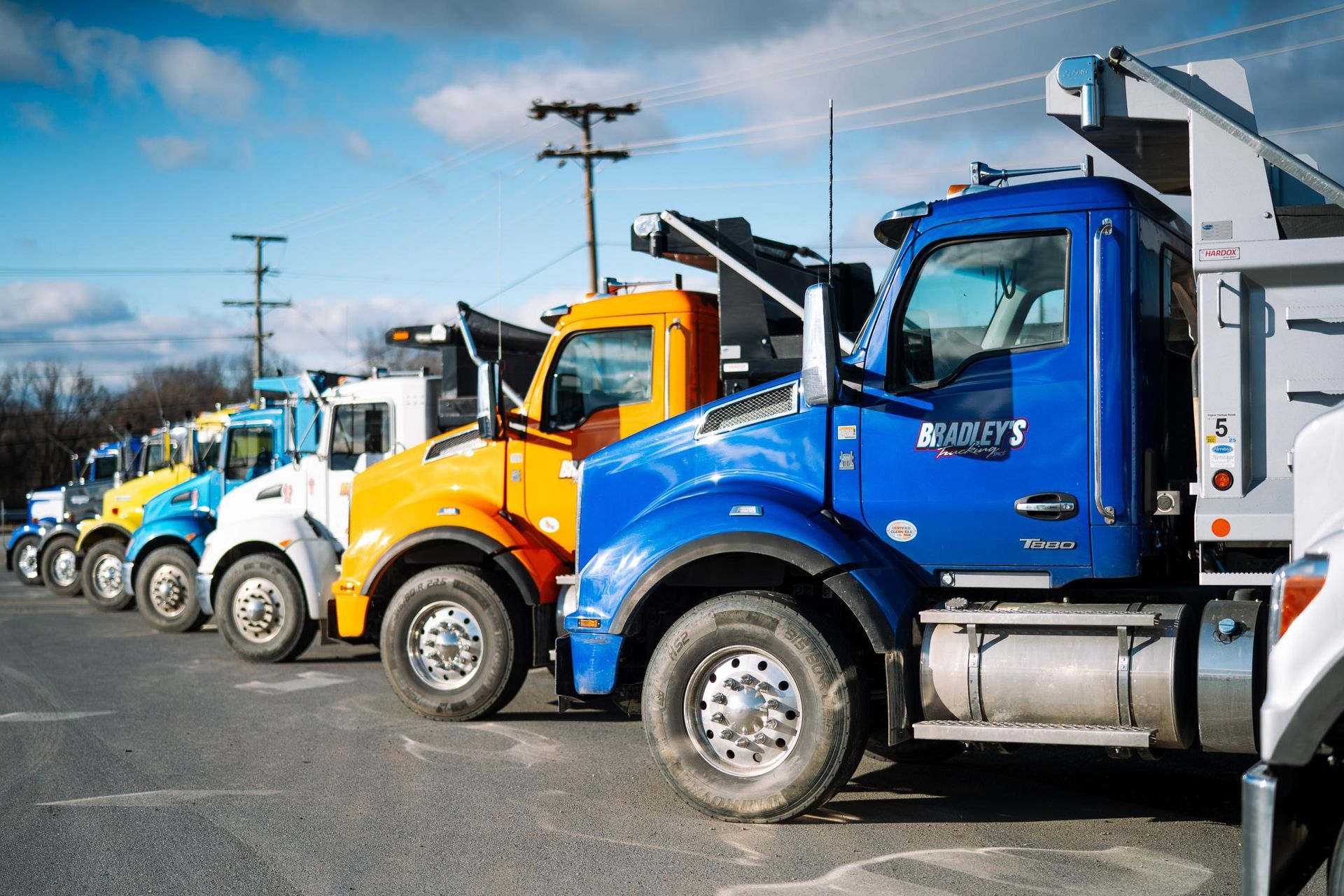 A row of dump trucks are parked in a parking lot.