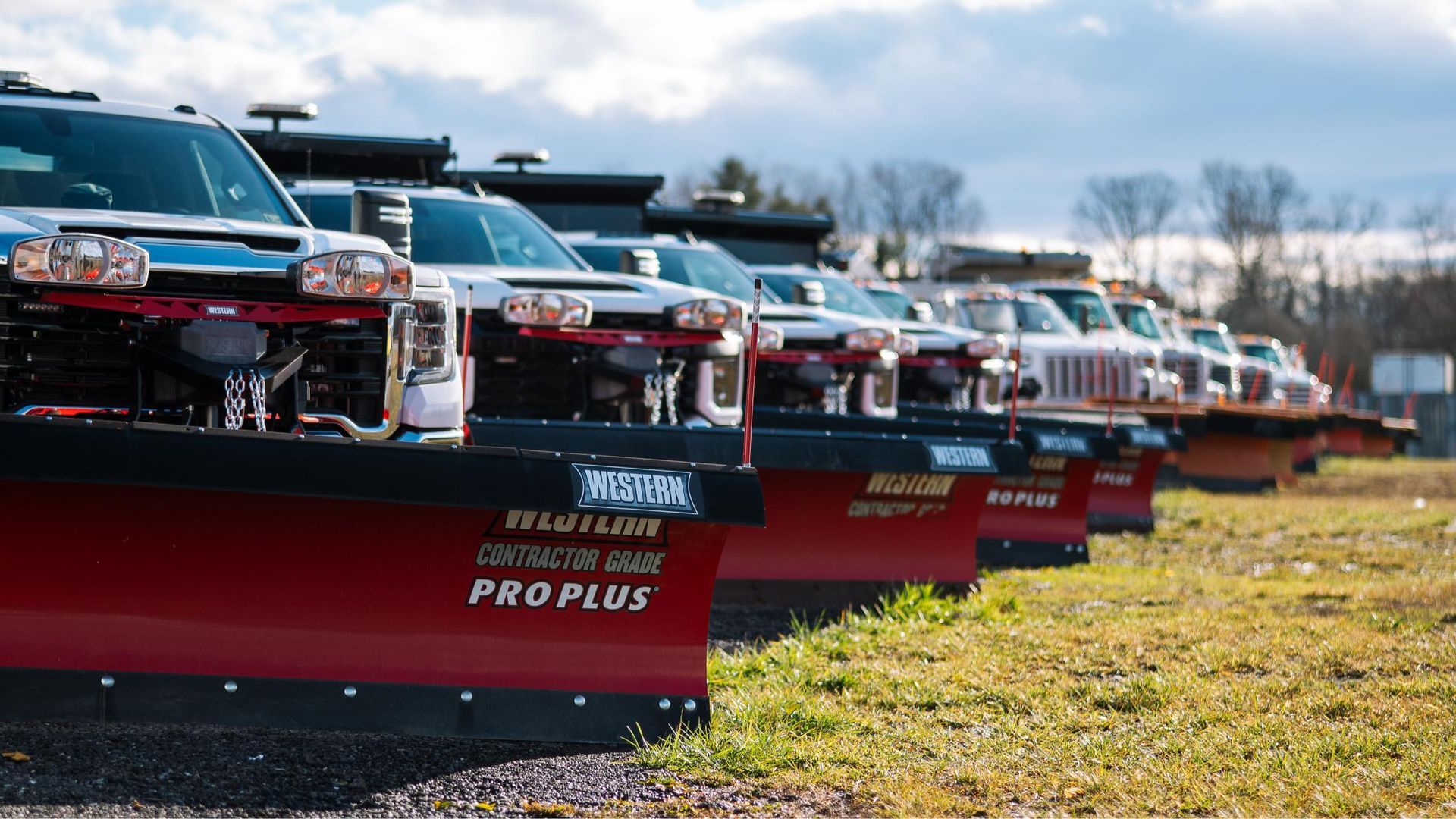 A row of snow plows are parked in a field.