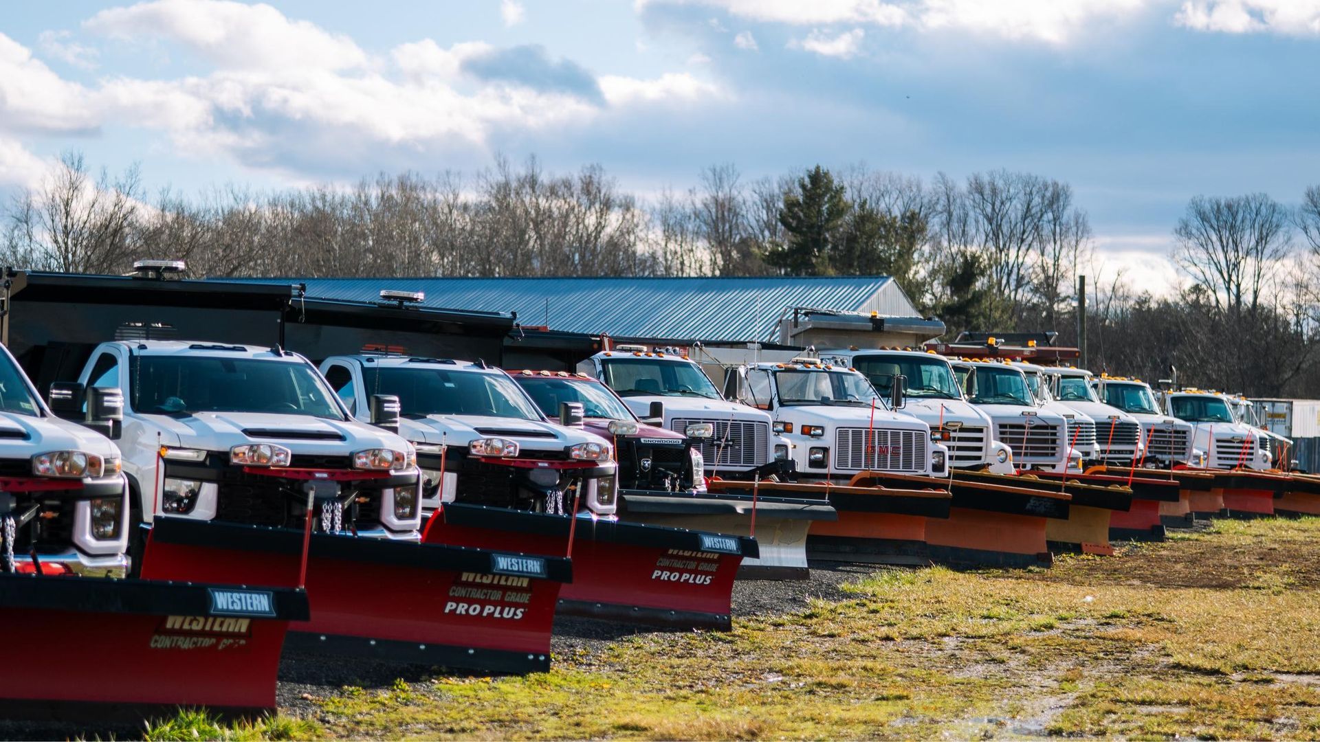 A row of snow plows are parked in a field.