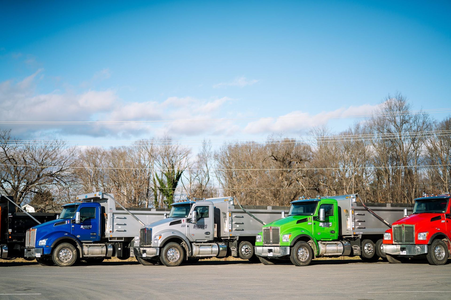 A row of dump trucks are parked in a parking lot.