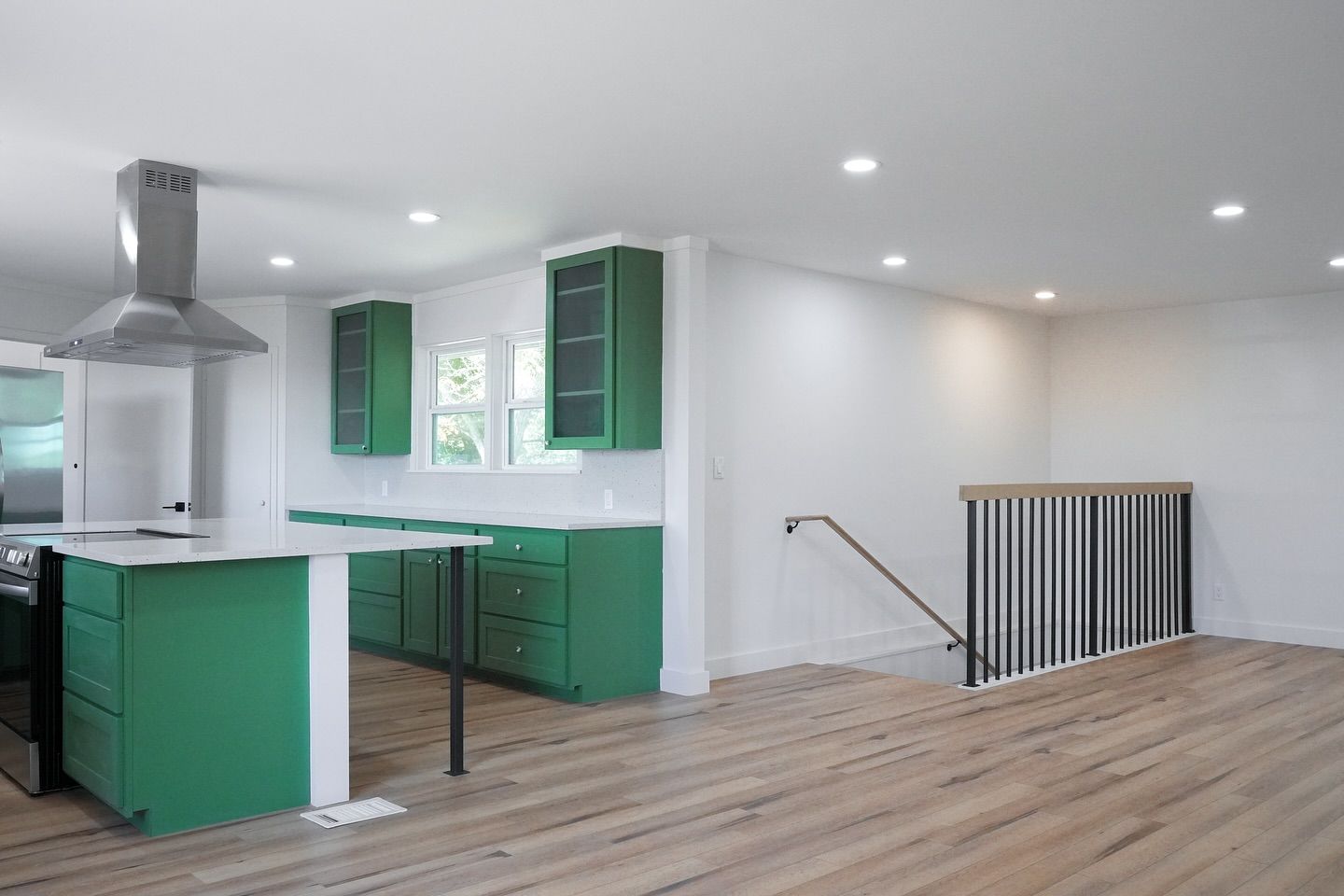 Green kitchen cabinets and island in a bright, open space with staircase.